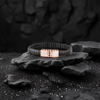 Black bracelet with rose gold clasp on a dark stone surface