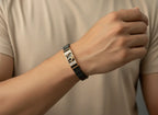 Person wearing a black and gold bracelet on a neutral background