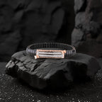 Black leather bracelet with rose gold clasp on a dark stone surface