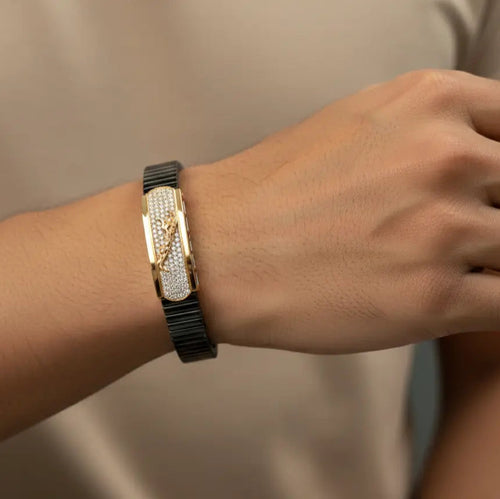 Hand wearing a black and gold bracelet on a neutral background