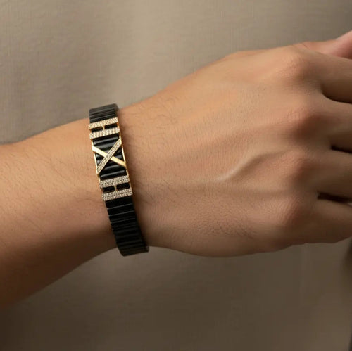Person wearing a black and gold patterned bracelet on a neutral background