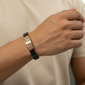 Hand wearing a black and gold bracelet on a plain background