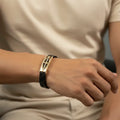 Person wearing a gold and black bracelet on a neutral background